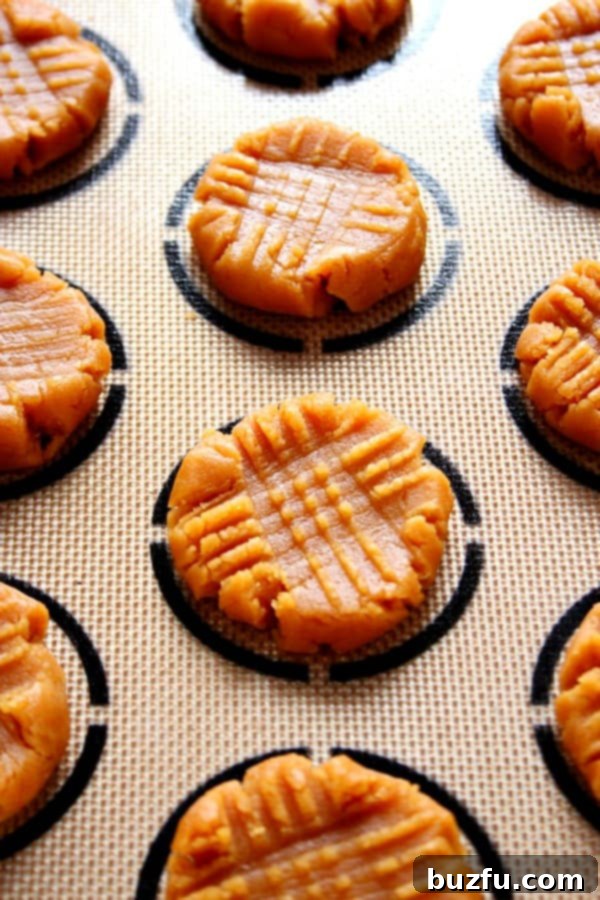 How to prepare classic peanut butter cookies without flour for baking. Side shot of flourless peanut butter cookie dough, neatly flattened in a criss-cross pattern on a silicone baking mat, ready for baking.
