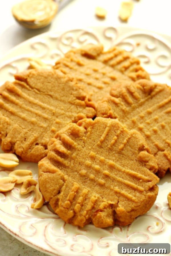 Flourless Peanut Butter Cookies - a simple classic from just 3 ingredients, no flour needed! Side shot of four perfectly baked flourless peanut butter cookies arranged on a simple white plate, ready to be enjoyed.