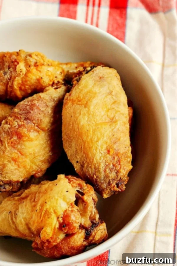 How to achieve crispy Buffalo chicken wings in the oven with a two-stage baking process. Overhead shot of perfectly crispy oven baked chicken wings glistening in a white bowl, ready for sauce.