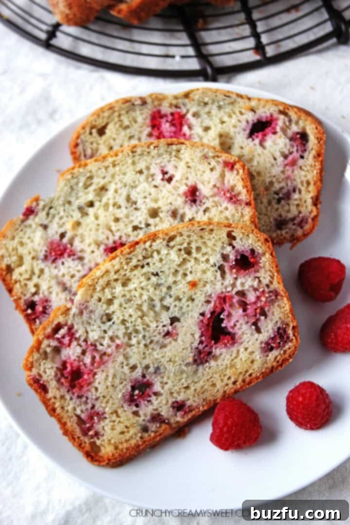 A beautifully golden-brown Lemon Raspberry Quick Bread loaf, sliced, revealing vibrant raspberries within.