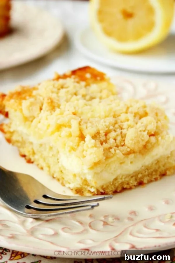 A delectable slice of Lemon Cream Cheese Crumb Cake on a white plate, showcasing its fluffy cake layer, creamy cheesecake center, and golden crumb topping.