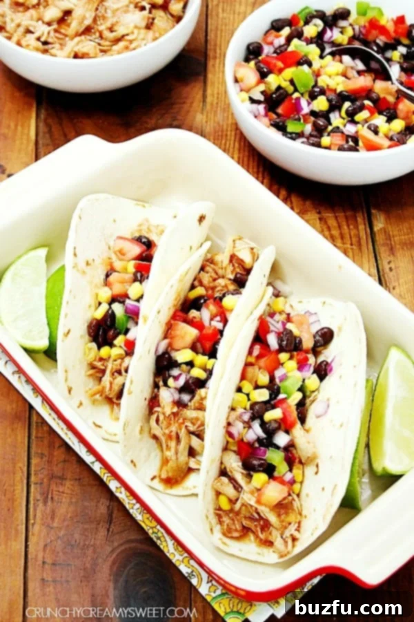 Three vibrant chicken tacos brimming with shredded chicken and fresh toppings, arranged attractively in a rustic baking dish.