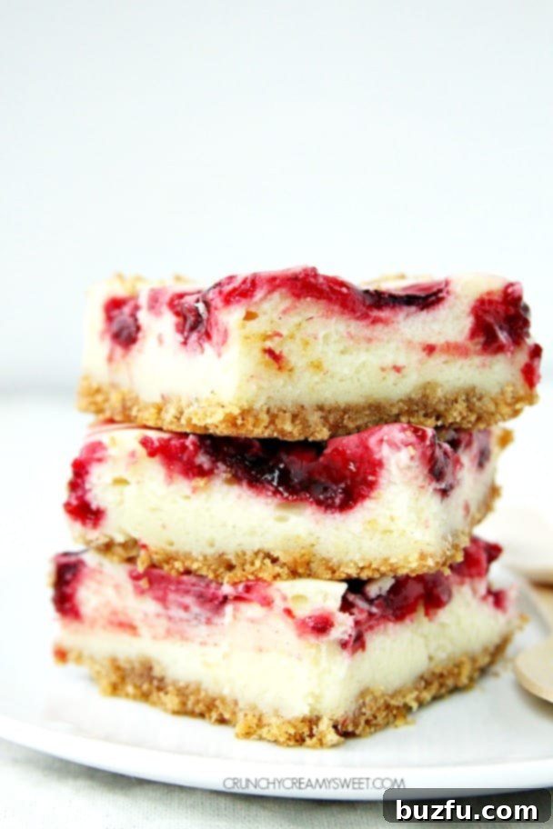 Side shot of three pieces of lemon raspberry cheesecake bars stacked up on each other. A delightful display of creamy, fruity dessert.