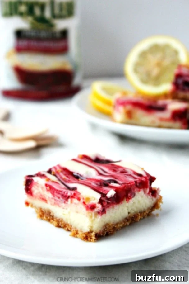 One piece of lemon raspberry cheesecake bar on a white plate, with more bars on another plate in the background, ready to be enjoyed.