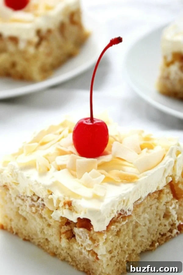 A perfectly sliced piece of Pina Colada Poke Cake on a white plate, showcasing layers of moist cake, pineapple-coconut filling, and creamy topping, garnished with a maraschino cherry and coconut flakes.