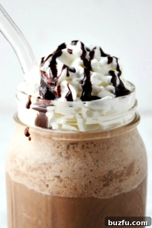 A close-up of a homemade Mocha Frappuccino in a clear mug, garnished with whipped cream and chocolate syrup.