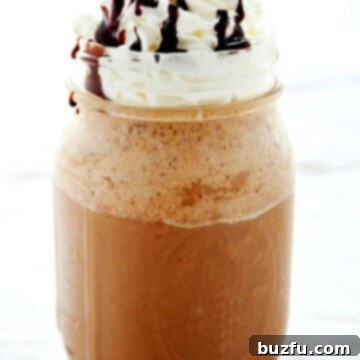 Homemade Mocha Frappuccino in a glass jar, topped generously with whipped cream and a chocolate drizzle.