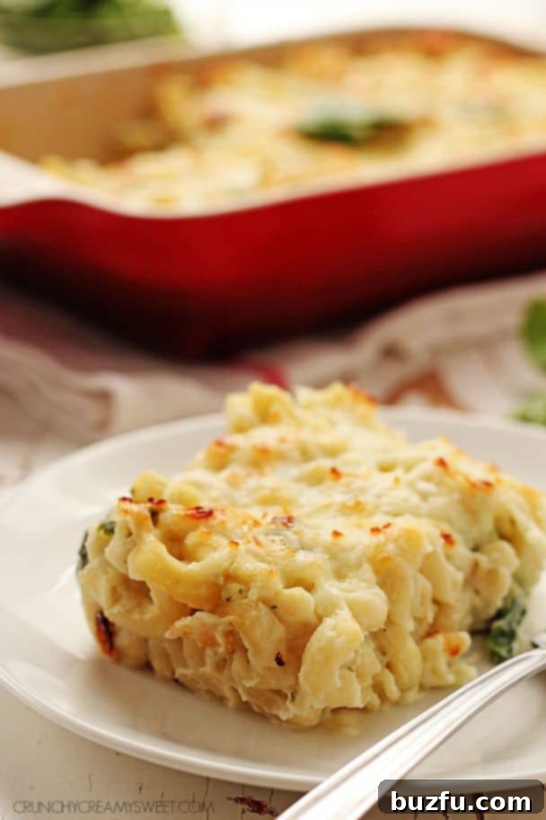 Piece of healthy mac and cheese on white plate with fork, baking dish with rest of mac in the background.