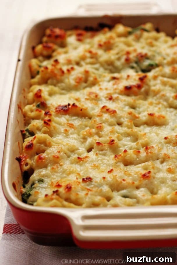 Side shot of healthy mac and cheese in rectangular dish, showing melted cheese and spinach.