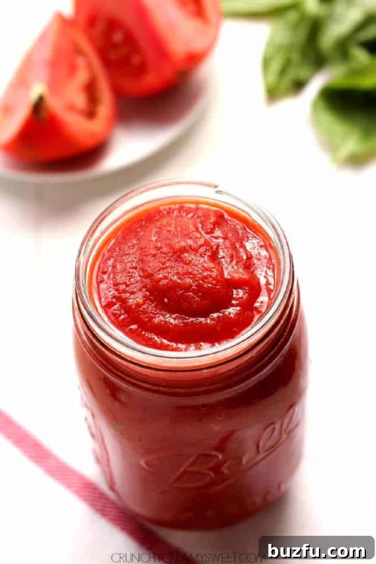 Smooth, vibrant red homemade tomato sauce presented elegantly in a clear glass jar, set against a pristine white background, perfectly showcasing its fresh quality and appealing texture.