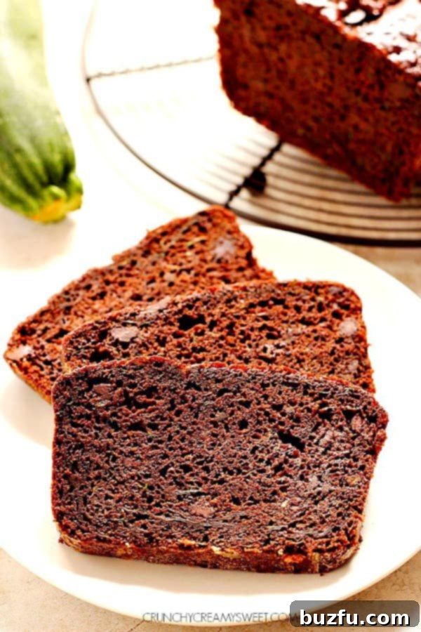 Three decadent slices of chocolate zucchini bread, rich brown with visible chocolate chips, arranged artfully on a white plate, ready to be enjoyed.