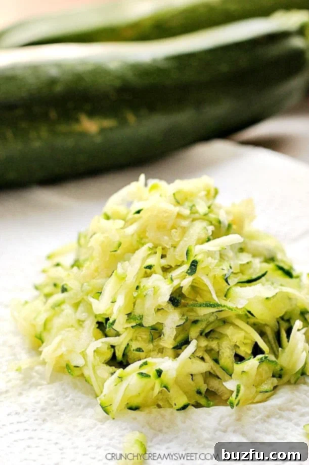A generous mound of freshly shredded zucchini placed on a paper towel, illustrating the crucial step of squeezing out excess moisture before baking.