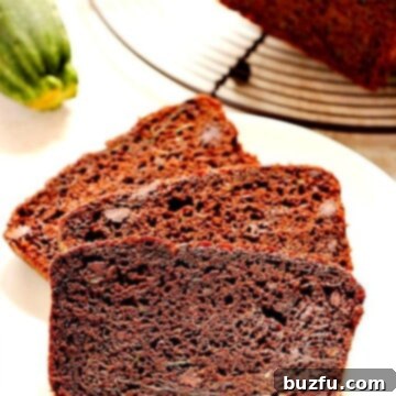 Slices of incredibly moist and rich chocolate zucchini bread on a clean white plate, garnished with a light dusting of powdered sugar.