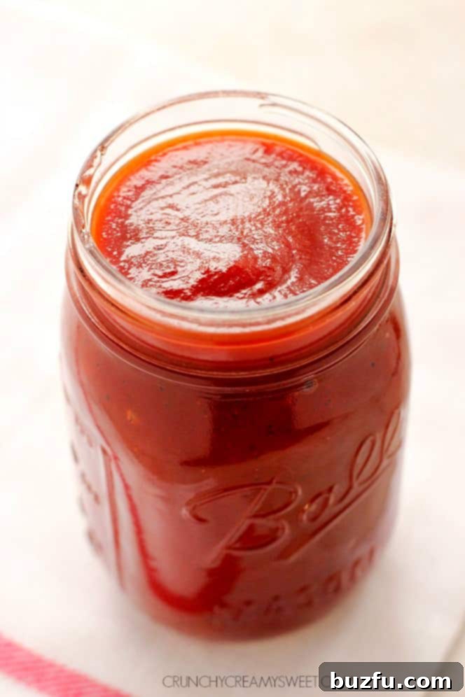 Side shot of rich, dark homemade BBQ sauce in a clear glass jar, ready for use or storage.