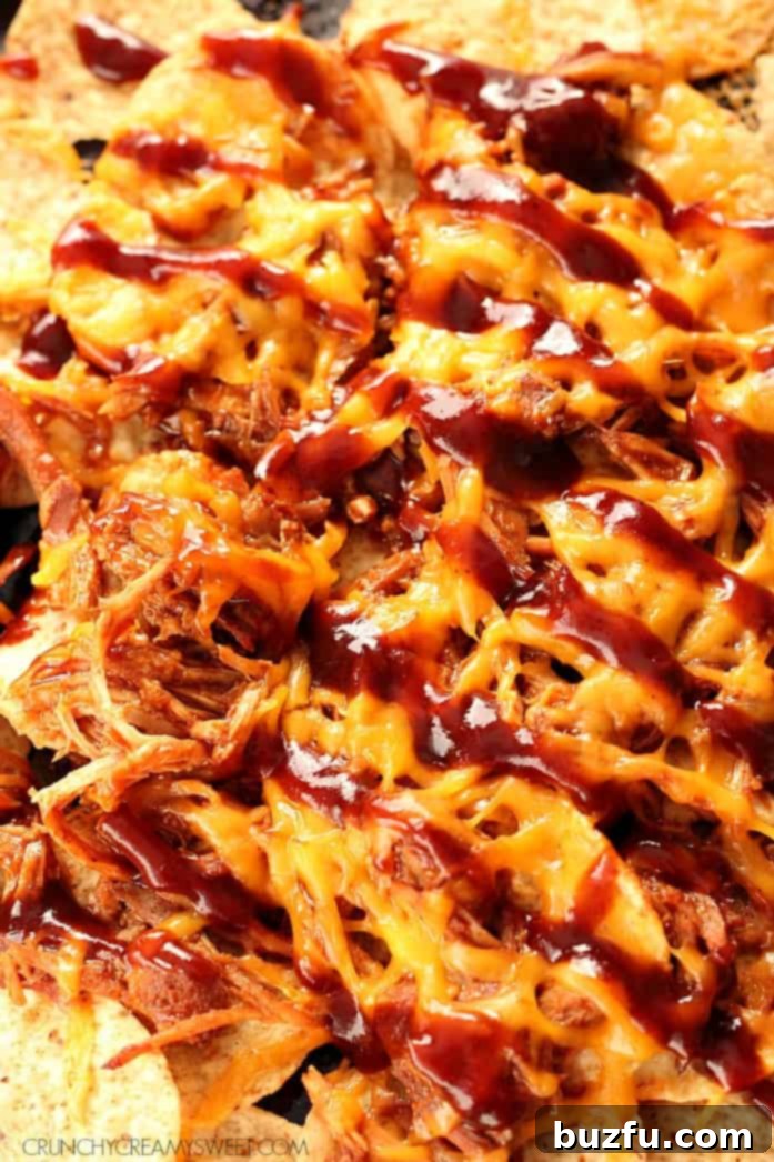 Pulled Pork Nachos with melted cheese and BBQ sauce on baking sheet.