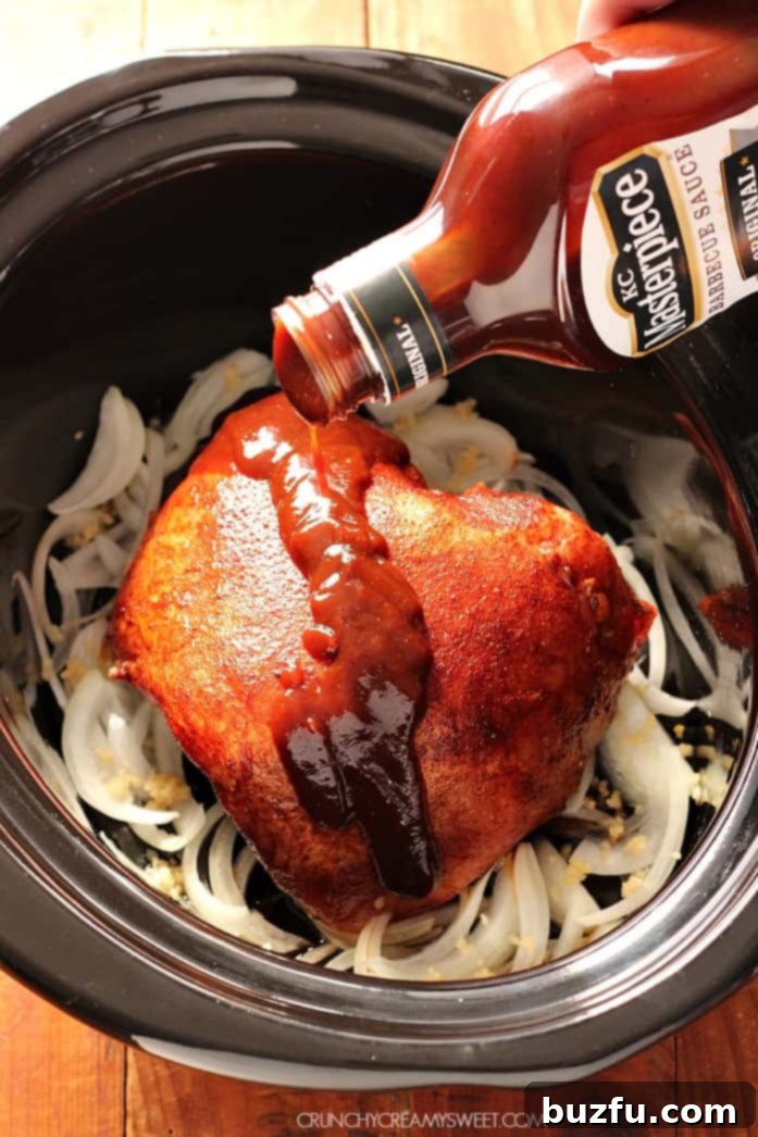 Overhead shot of BBQ sauce being poured over pork roast in slow cooker, illustrating the preparation step.