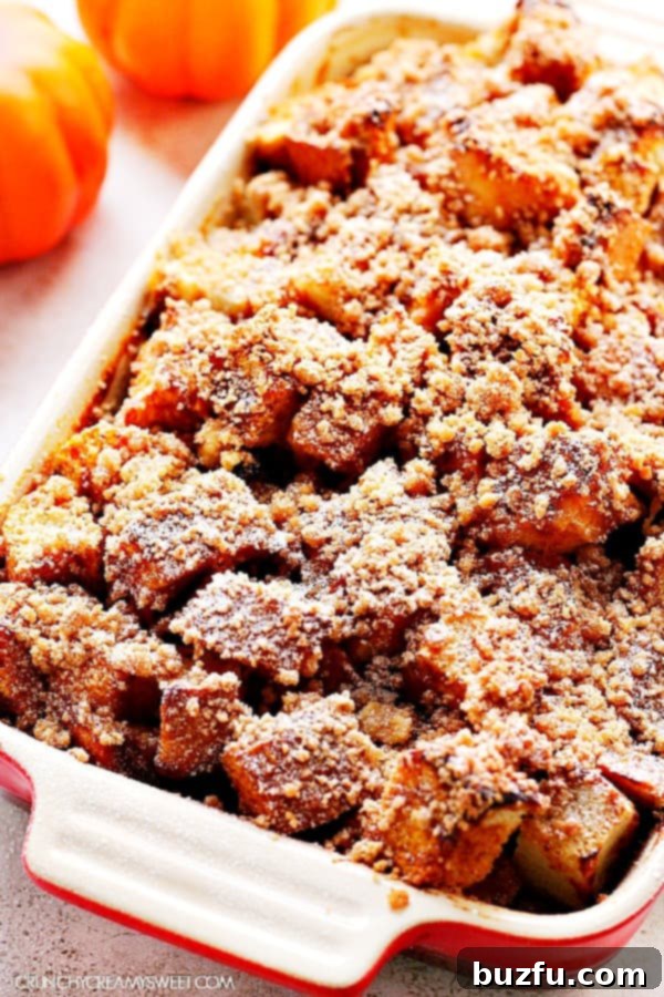 A golden-brown Pumpkin French Toast Casserole, freshly baked in a ceramic baking dish, ready to be served. The top is covered with a delicious crumb topping and the sides show the custardy bread.