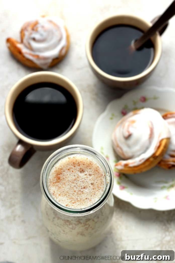 Freshly prepared Homemade Cinnamon Roll Coffee Creamer served with morning coffee. Overhead shot of homemade coffee creamer in a tall glass bottle and coffee in two matching coffee cups, ready to be enjoyed.