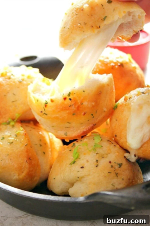Garlic Cheese Bombs in mini cast iron skillet, one pulled apart with gooey center shown.