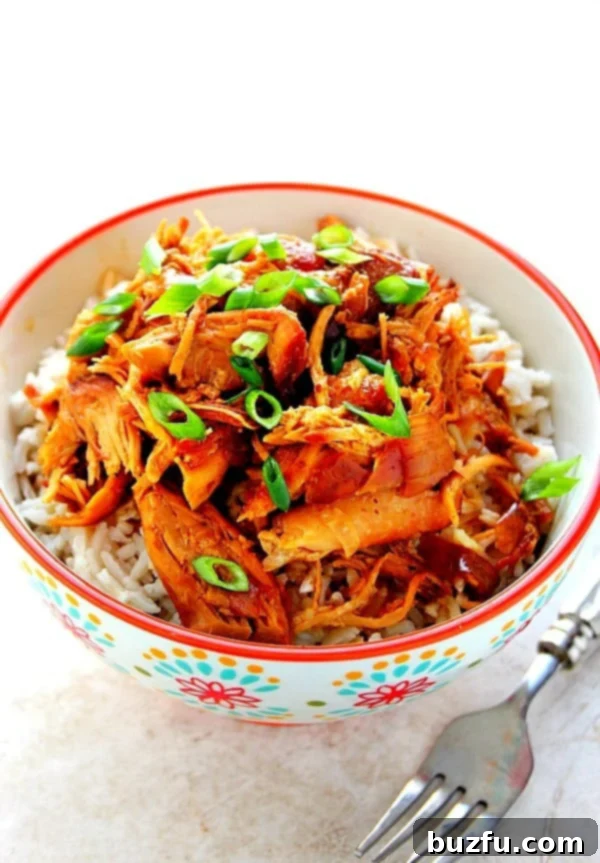 How to make crock pot teriyaki brown sugar chicken. Perfect served over rice and steamed vegetables! Overhead shot of shredded cooked teriyaki chicken over rice in bowl with red rim, garnished with green onions.