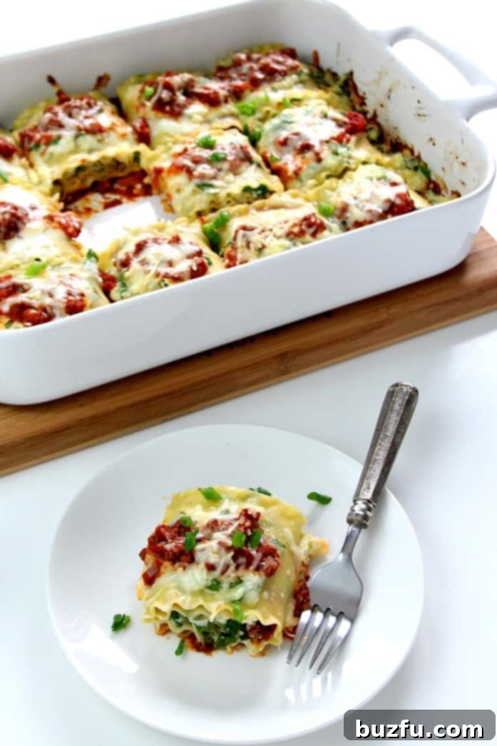 Spinach Lasagna Roll Ups - classic dish with a twist! Spinach lasagna roll ups are easy, delicious, elegant and fun to eat! Overhead shot of golden-baked spinach lasagna roll-ups nestled in a baking dish, with one perfect roll-up on a white plate, ready to be enjoyed with a fork.