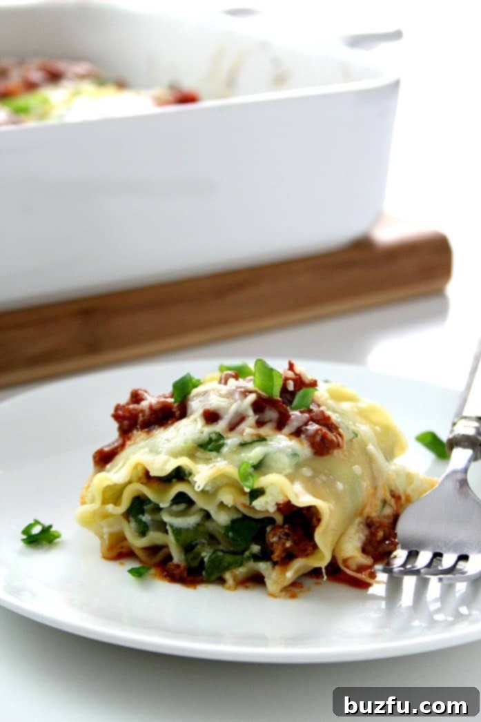Spinach Lasagna Roll Ups - classic dish with a twist! Spinach lasagna roll ups are easy, delicious, elegant and fun to eat! A close-up side view of a single, perfectly golden-baked spinach lasagna roll-up on a white plate, showcasing its layered filling.