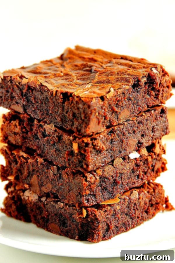 Side shot of four rich, fudgy brownie squares stacked on top of each other, showcasing their perfect texture and flaky top.