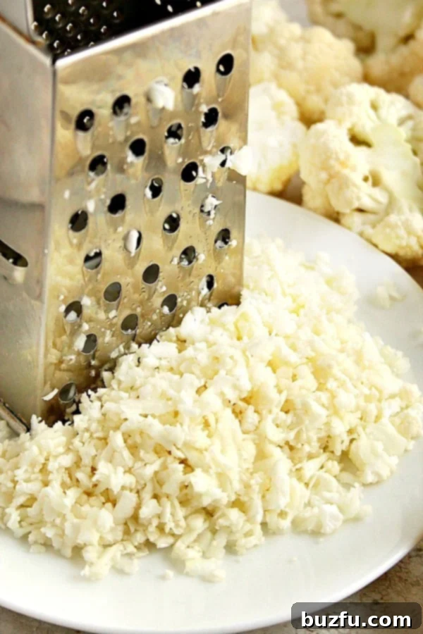 Fresh cauliflower being grated on a box grater into a white plate, highlighting the 'rice' texture.