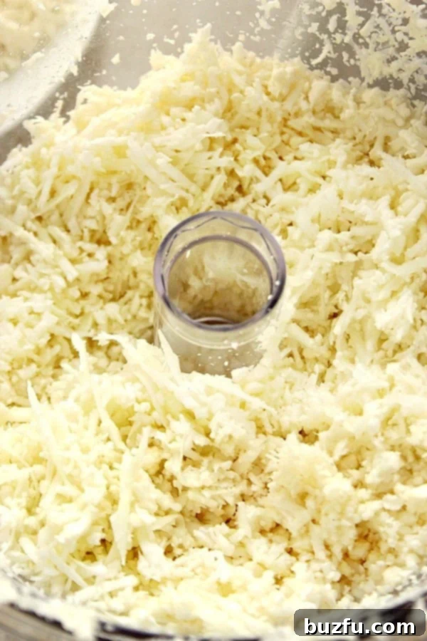 Close up shot of grated cauliflower florets in a food processor bowl, demonstrating the 'rice' texture.