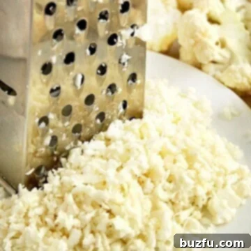 Grater with cauliflower rice on white plate, illustrating the raw product.