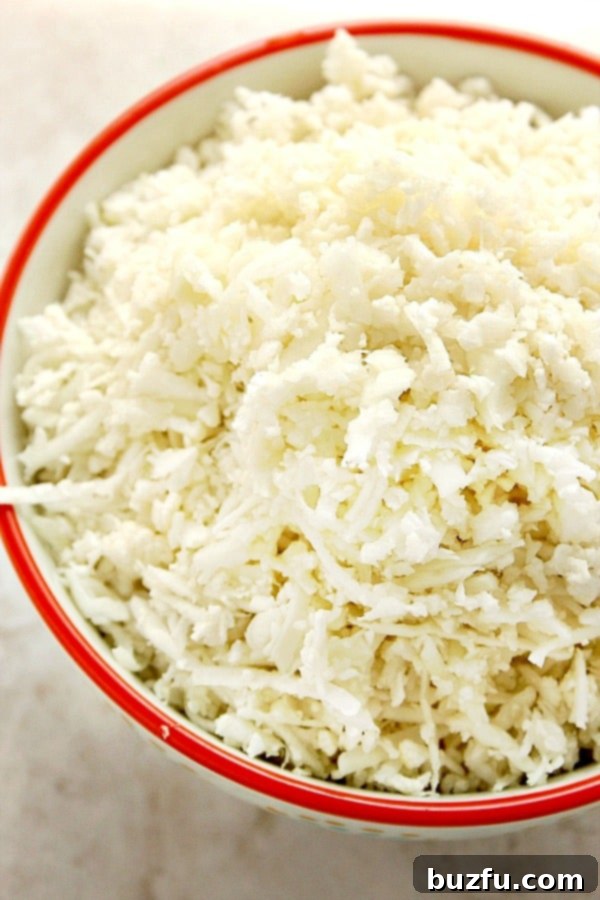 A close-up view of cauliflower rice in a white bowl with a red rim, illustrating its texture before cooking.
