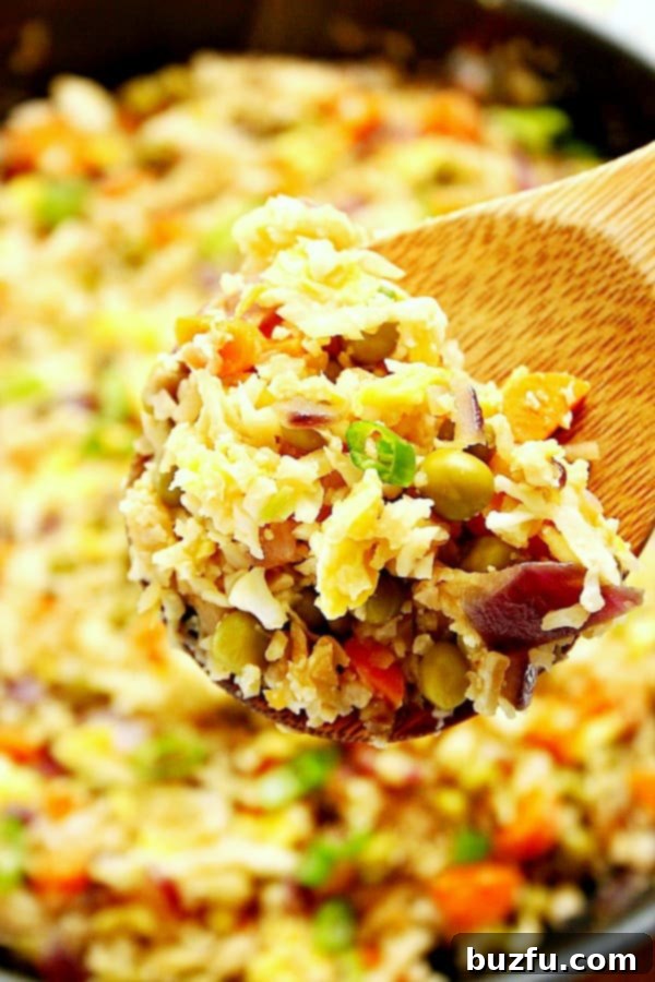 Close-up of fluffy and flavorful cauliflower fried rice served on a wooden spoon, highlighting its satisfying texture and vibrant ingredients.