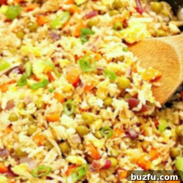 Cauliflower fried rice in skillet, with wooden spoon, showcasing the delicious result.