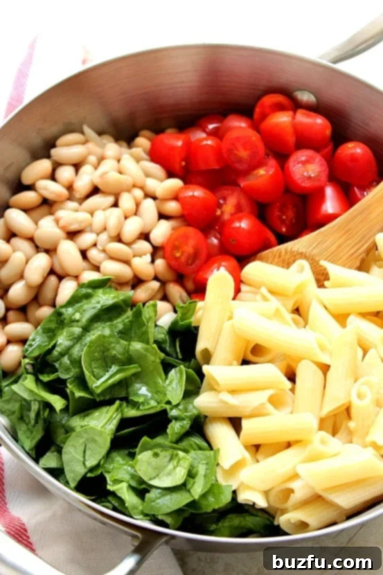 Various ingredients for skillet pasta including penne, tomatoes, spinach, and beans neatly arranged in a skillet.