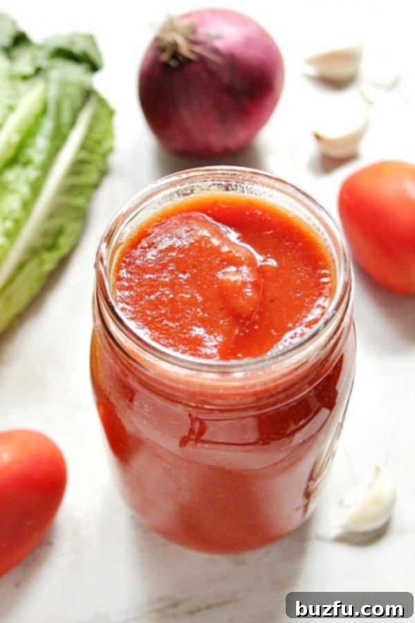 Red sauce in glass jar, with vegetables around it.