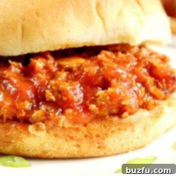 Side shot of Sloppy Joes in bun on white plate.