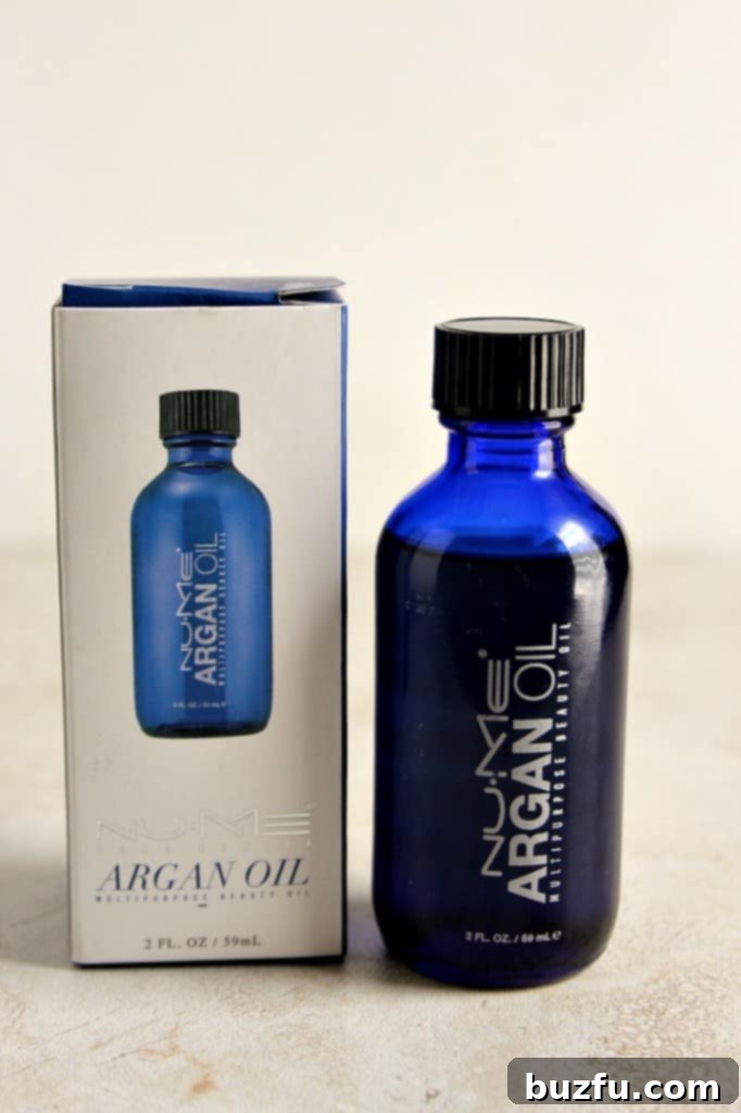 A full-size bottle of NuMe Argan Oil, emphasizing its value as a free gift with the curling wand purchase, highlighting its benefits for hair health and shine.