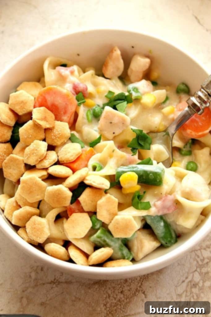 Overhead shot of chicken pot pie pasta with oyster crackers in white bowl, highlighting the vibrant colors of the vegetables and the creamy sauce.