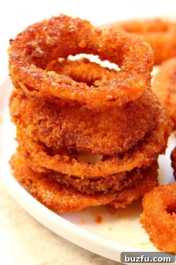 Zesty Buffalo Onion Rings 3 Close-up of golden brown, perfectly fried buffalo onion rings stacked on a plate.