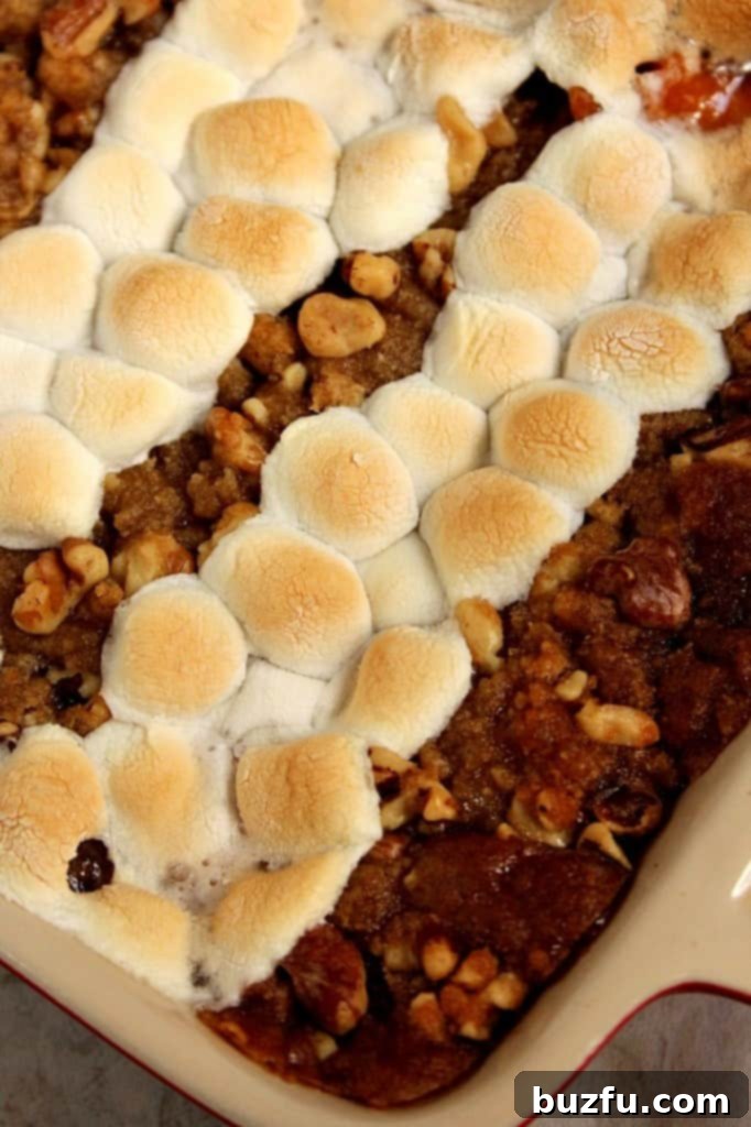 A vibrant sweet potato casserole with a dual topping of golden praline and fluffy toasted marshmallows, ready for a Thanksgiving dinner.