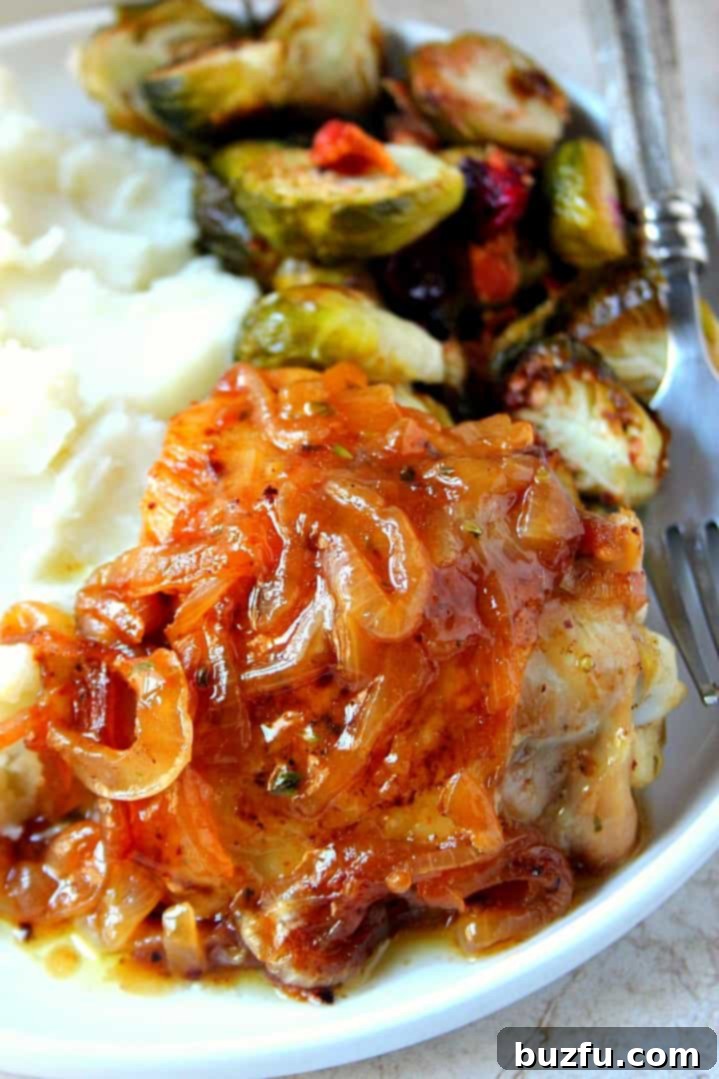 French Onion Roasted Chicken Recipe - combining two classic comfort foods into one incredibly indulgent and satisfying dish. Each piece is juicy and flavorful. Close up shot of a perfectly roasted French onion chicken thigh on a white plate, garnished with fresh herbs, alongside roasted Brussels sprouts.