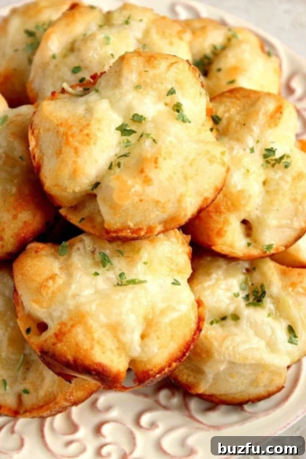 Golden brown garlic parmesan pull-apart rolls stacked on a white plate, garnished with fresh parsley.