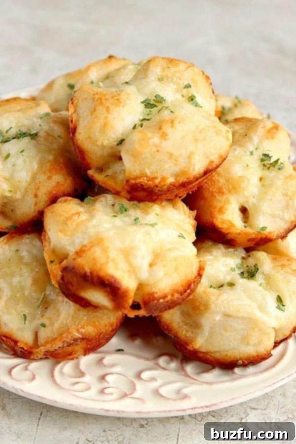 Close-up of several baked garlic parmesan pull-apart rolls on a white plate, showing melted cheese and golden edges.