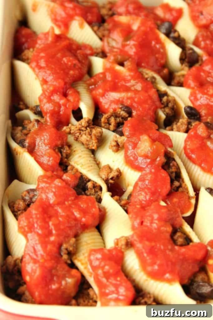An overhead view of Taco Stuffed Pasta Shells baking in a casserole dish, topped with melted cheese and rich tomato sauce.