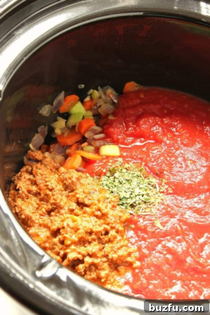 A slow cooker filled with all the delicious ingredients for Bolognese sauce, including browned beef, diced vegetables, crushed tomatoes, and seasonings, before slow cooking.