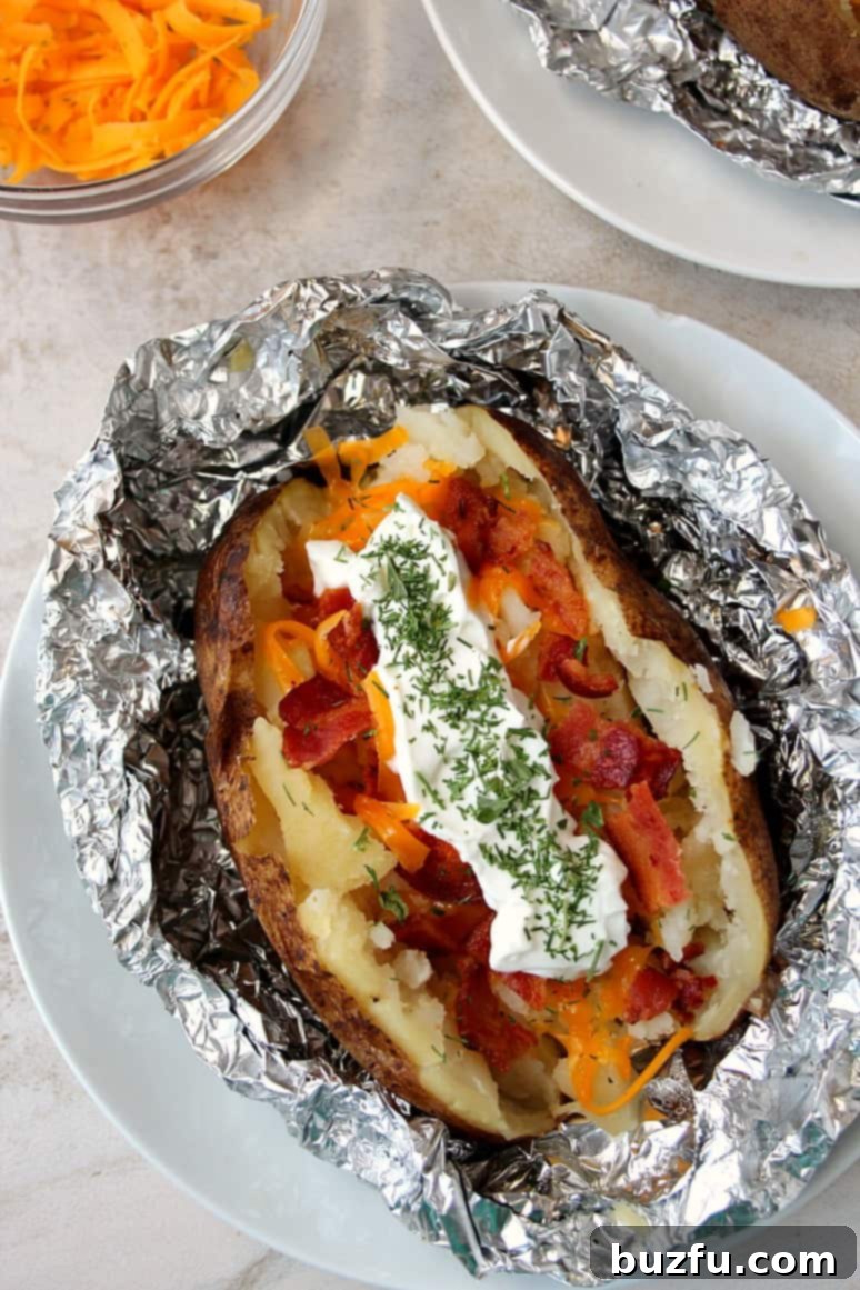 Slow Cooker Baked Potatoes Recipe - perfectly soft and fluffy potatoes baked in a crock pot. So easy and perfect topped with cheese, bacon and sour cream. Overhead shot of baked potato in foil, topped with bacon, cheese and sour cream, set on white plate.