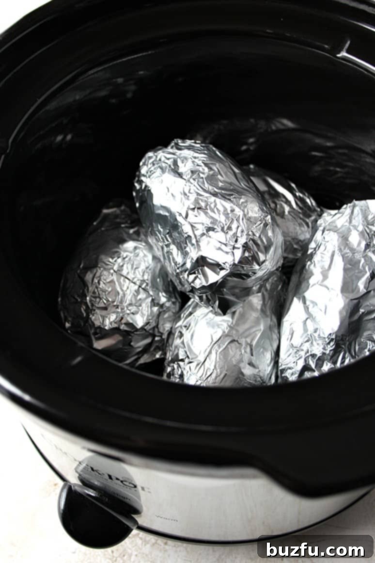 How to make baked potatoes in a slow cooker Side shot of potatoes wrapped in foil, set in slow cooker.