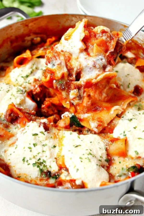 Close up shot skillet lasagna on spoon over pan, showing layers of noodles, sausage, and melted cheese.