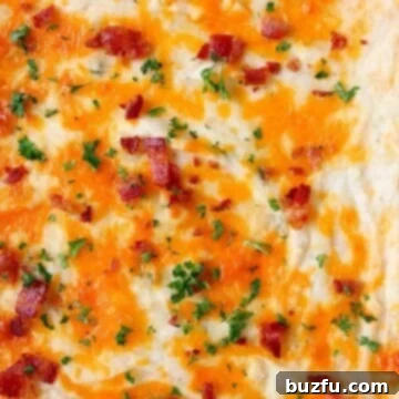 A close-up of the gooey, melted cheddar cheese on top of the mashed potato casserole, with crispy bacon bits sprinkled over it.