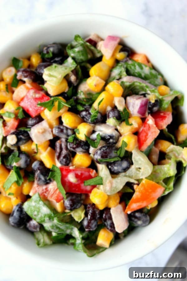 Vibrant Black Bean Taco Salad in a white bowl, garnished with fresh herbs and a drizzle of creamy dressing.